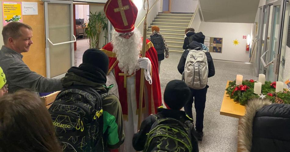 HL Nikolaus verteilt im Eingangsbereich der Mittelschule Geschenke an die ankommenden Schüler:innen